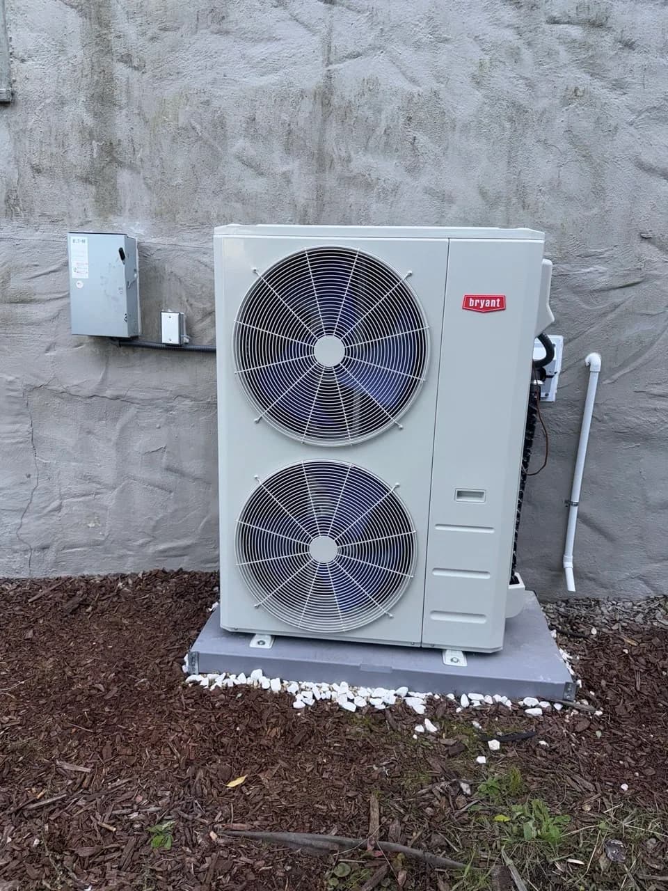 New heat pump outdoor unit set on a level pad beside the house